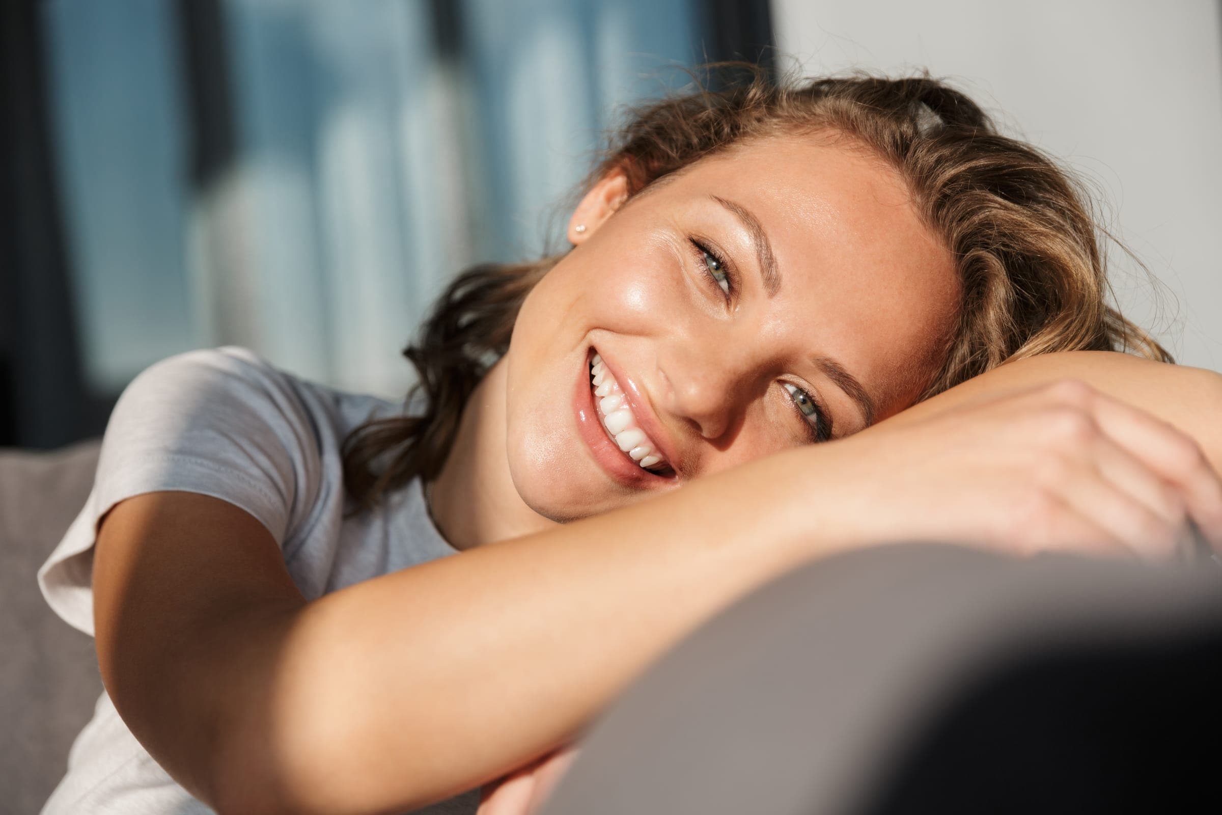 A patient leaning over a couch, smiling warmly into sunlight.