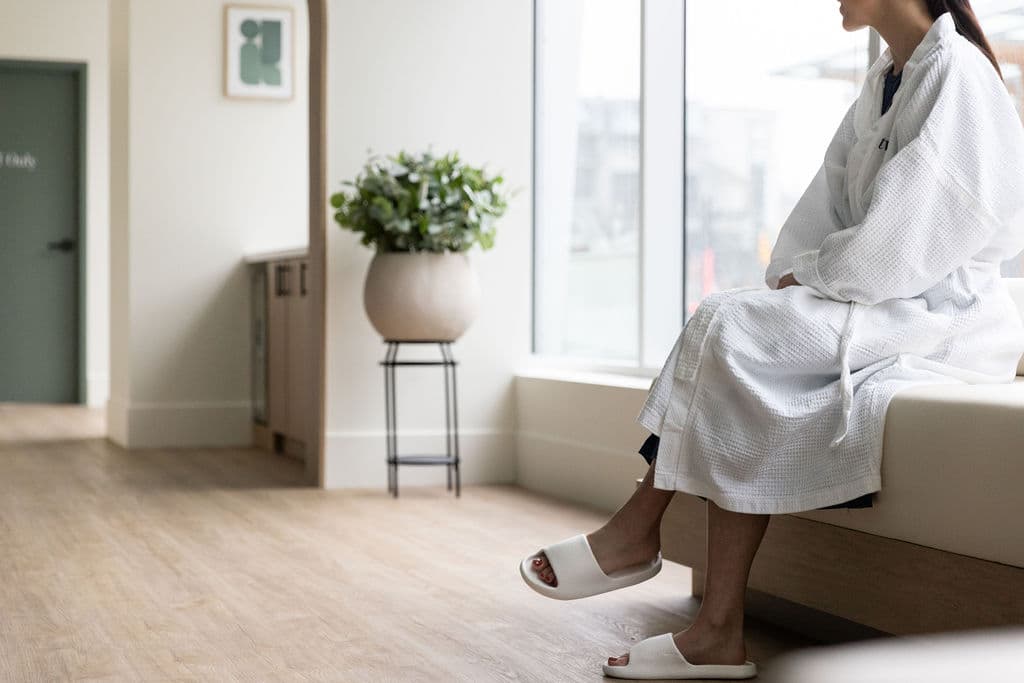 A patient sitting by a window in a soft robe, waiting for a Fertility Check appointment.