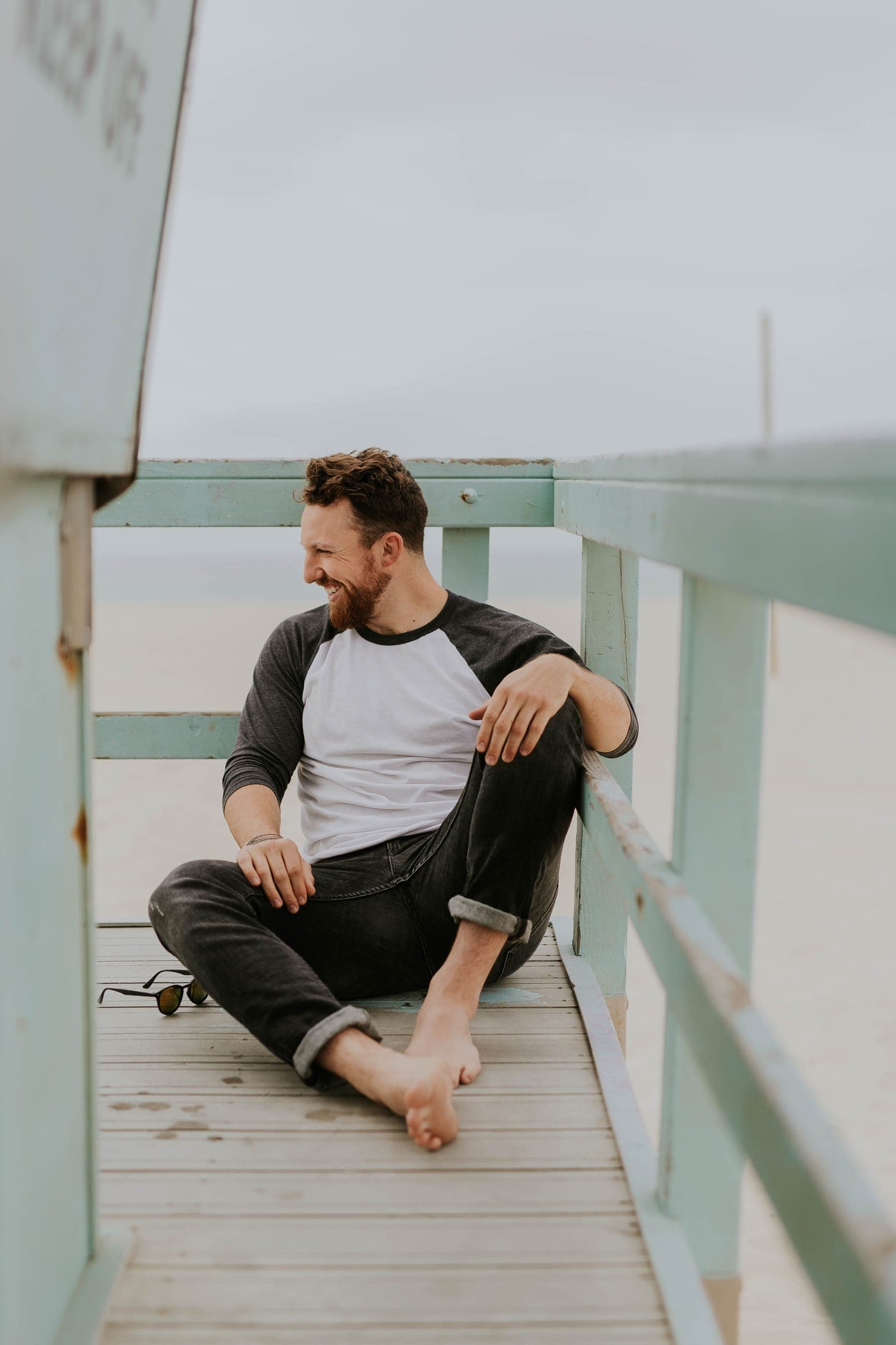 A man laughing under a lifeguard tower at the beach.