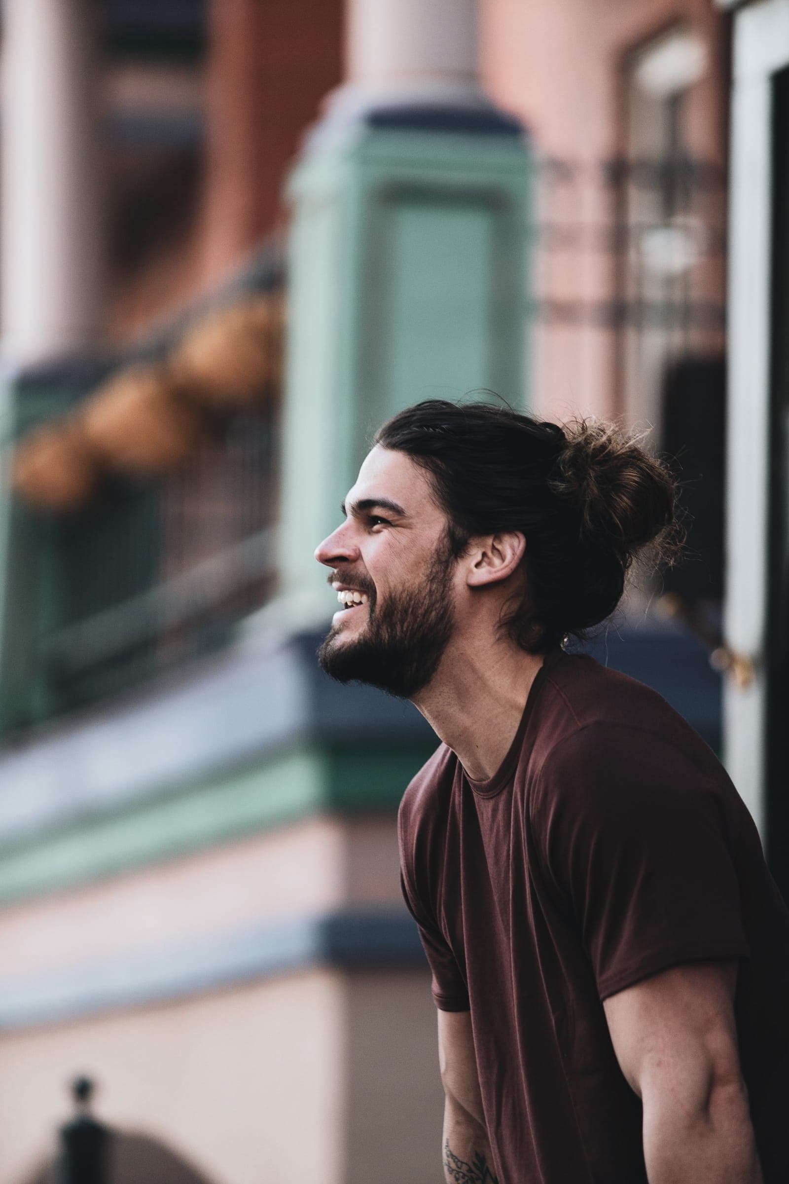 A man laughing on a sunny street, looking off to the side.